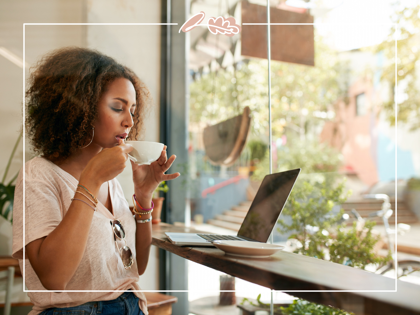 Woman sipping coffee while sitting at a café window with a laptop. Fabulous Flowers and Gifts