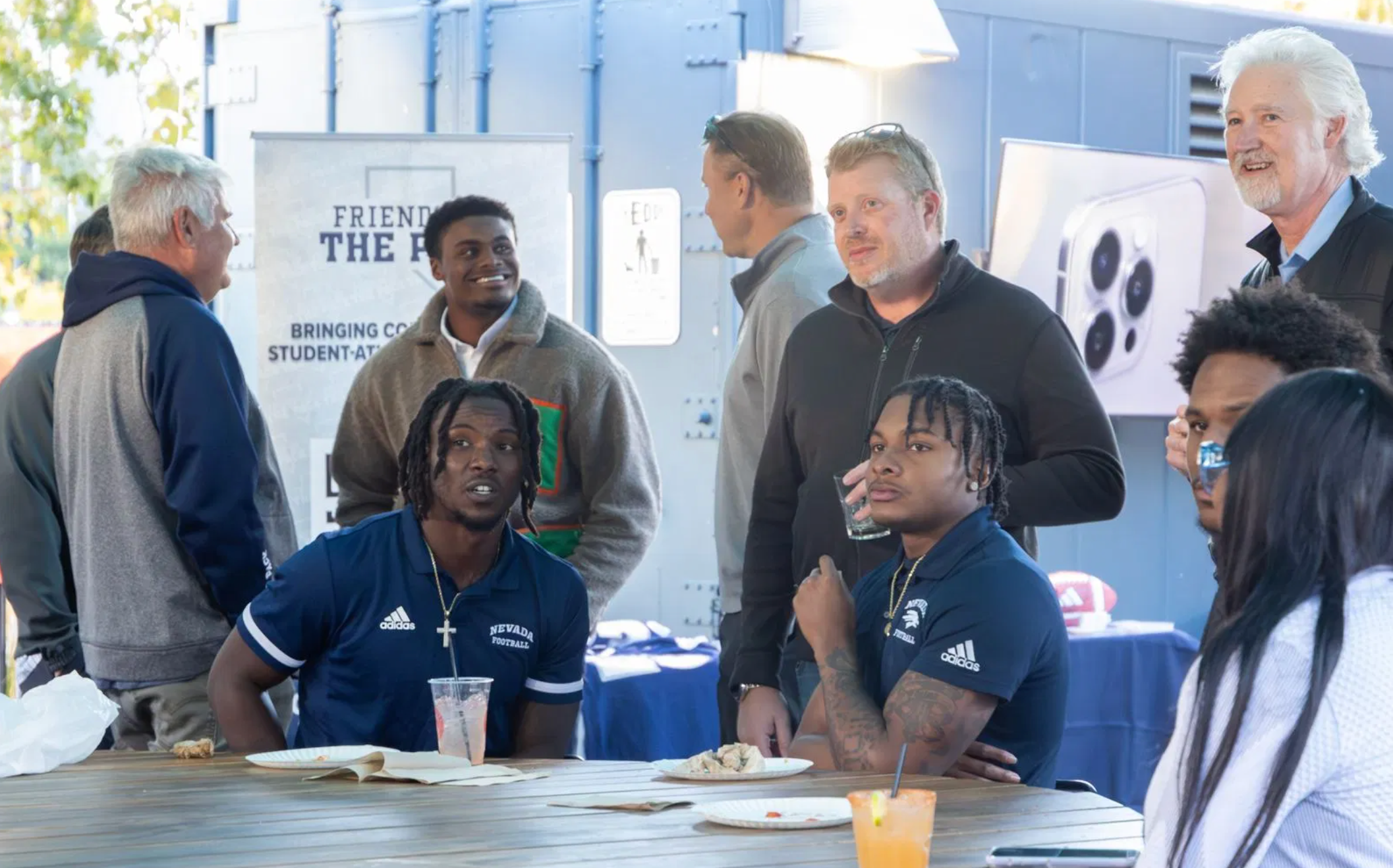 Nevada football players seated at a table with alumni and business professionals during an NIL networking mixer, highlighting community efforts to support student-athlete brand opportunities.