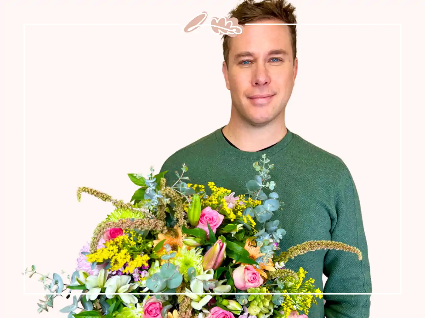 A man in a green sweater holding a colorful bouquet of flowers, including pink roses and yellow accents, against a white background. Fabulous Flowers and Gifts.