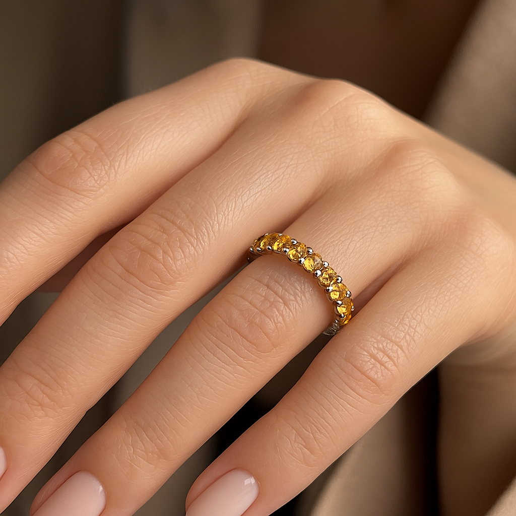 Moteriška ranka su žiedu juostele iš geltono aukso, puošta geltonais safyrais ir mažais deimantais, skleidžiančiais šiltą švytėjimą.