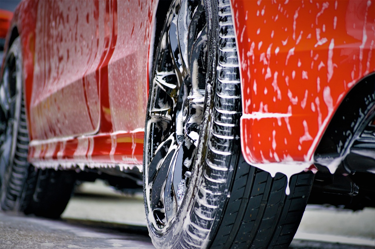 Closeup of red car with soap dripping off frame and tires