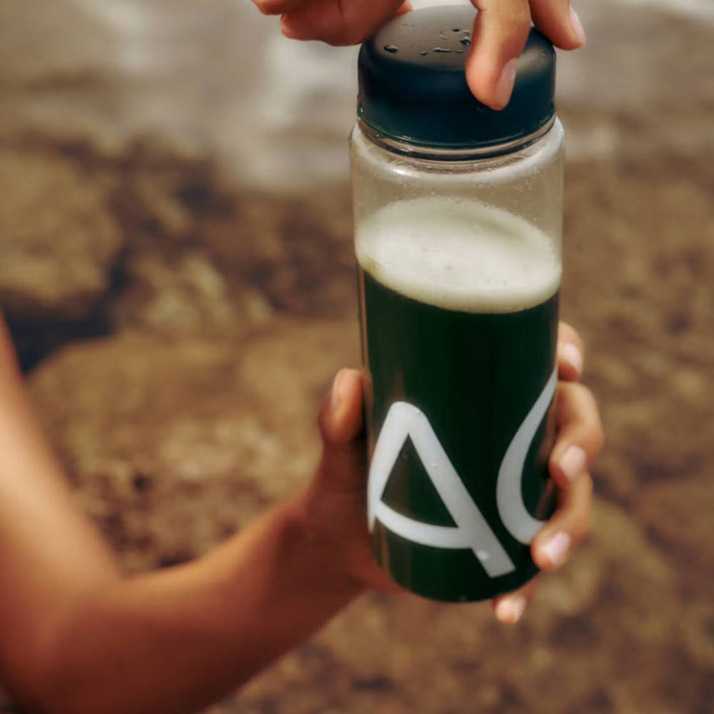 A person holding a bottle of Athletic Greens.