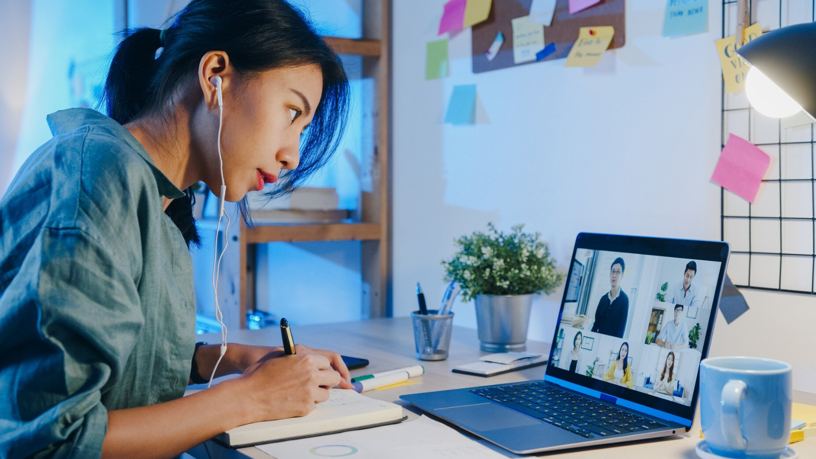 Focused woman taking notes during a virtual meeting, capturing hybrid engagement and weekly team updates.