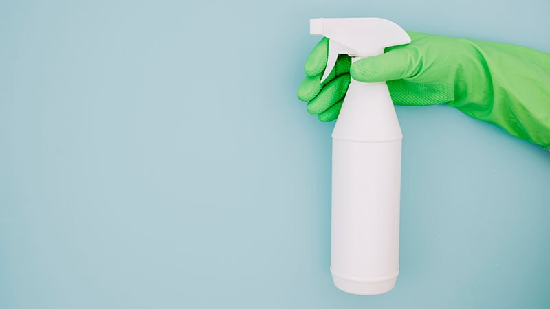 Hand in green glove holding disinfecting spray bottle