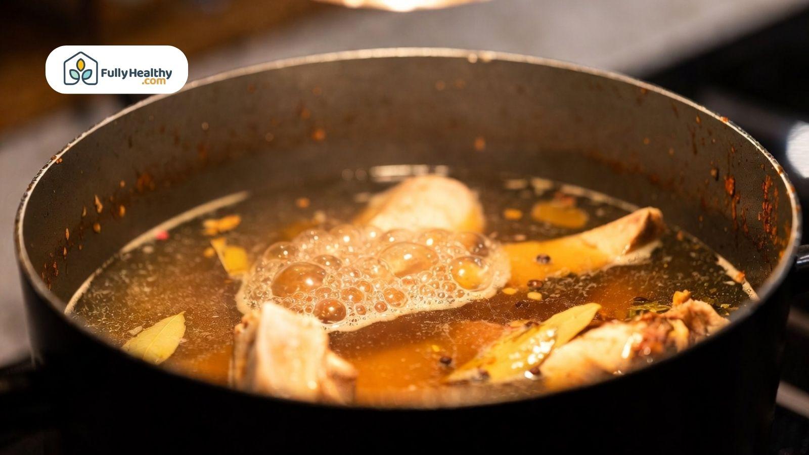 Close-up of bone broth simmering in a pot with bones and spices visible.