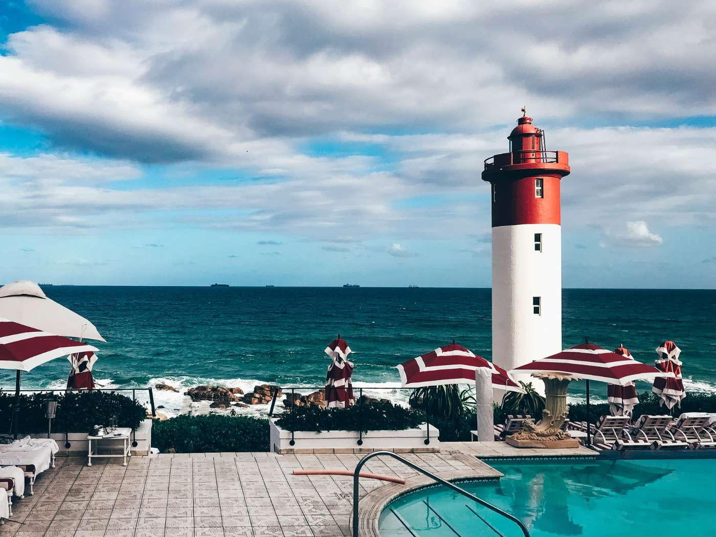 Iconic red and white lighthouse overlooking the ocean with poolside umbrellas in Durban, reflecting the extensive range of the Durban Gift Box Delivery Collection suitable for family and wine hampers, offering a thoughtful selection of gifts by Fabulous Flowers and Gifts.