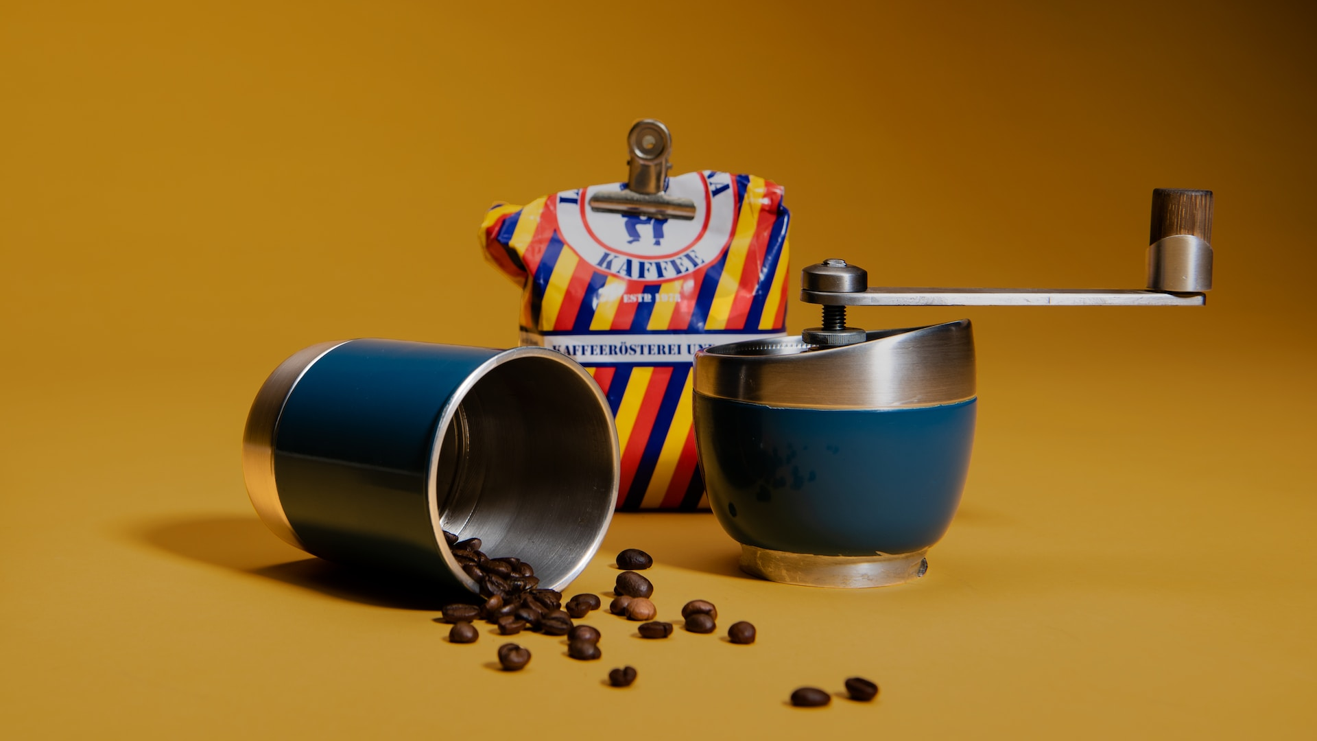 A small, blue handheld coffee grinder tipped over with coffee beans coming out of it