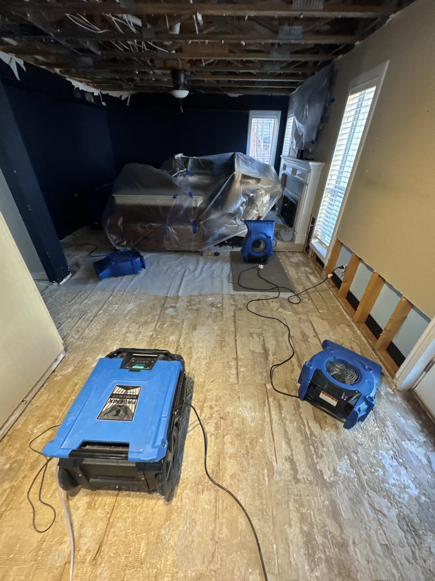 A commercial dehumidifier and air movers are actively drying a hallway floor affected by water damage, showcasing the water damage restoration process. This equipment is essential for mitigating moisture and preventing mold growth in the property.