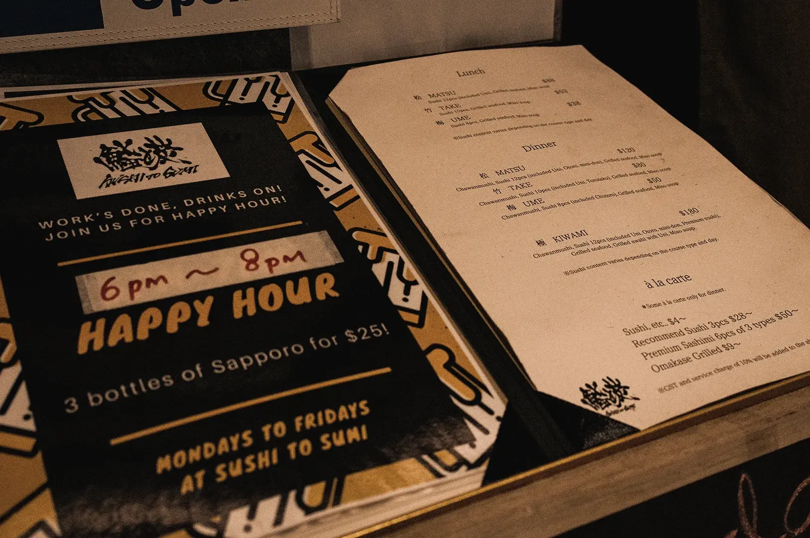 A high-angle close-up shot features the printed omakase set menus alongside a Happy Hour beer promotion flyer at Sushi to Sumi in Raffles Place.