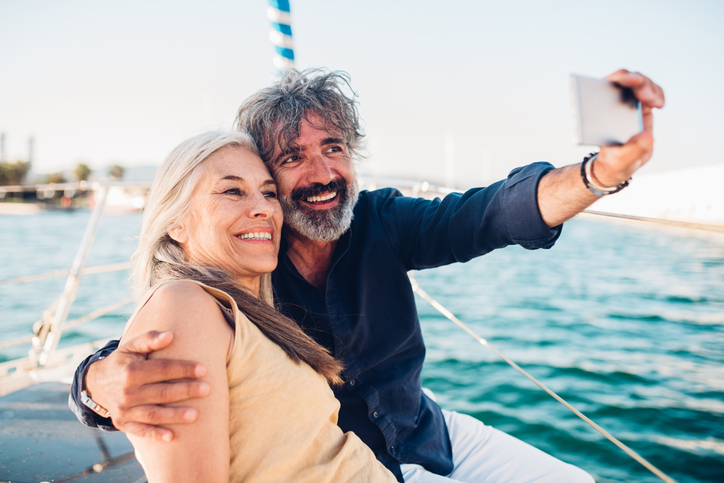 Gray haired woman and man in a blue shirt smiling for a selfie on a boat.
