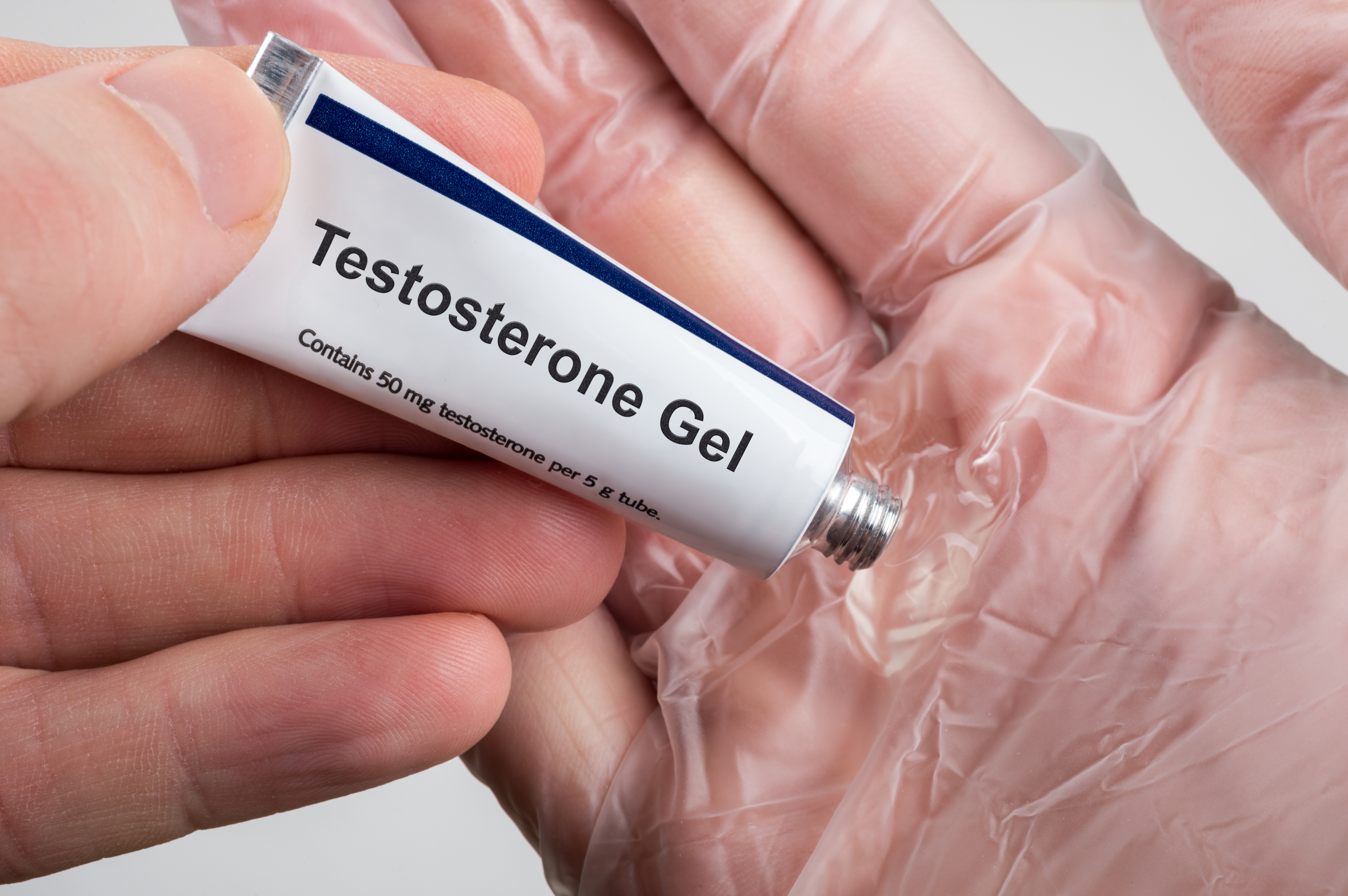 Caucasian hand holding a tube marked as "testosterone gel", squeezing it into the palm of the other hand 