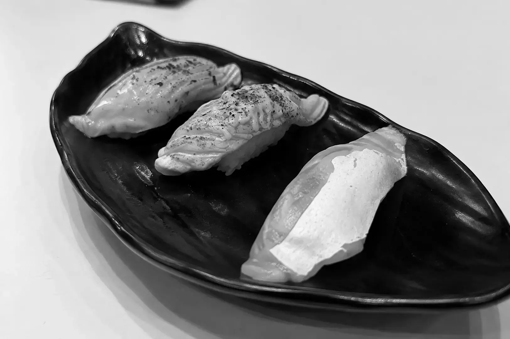 Trio of premium nigiri sushi served on a black ceramic plate.