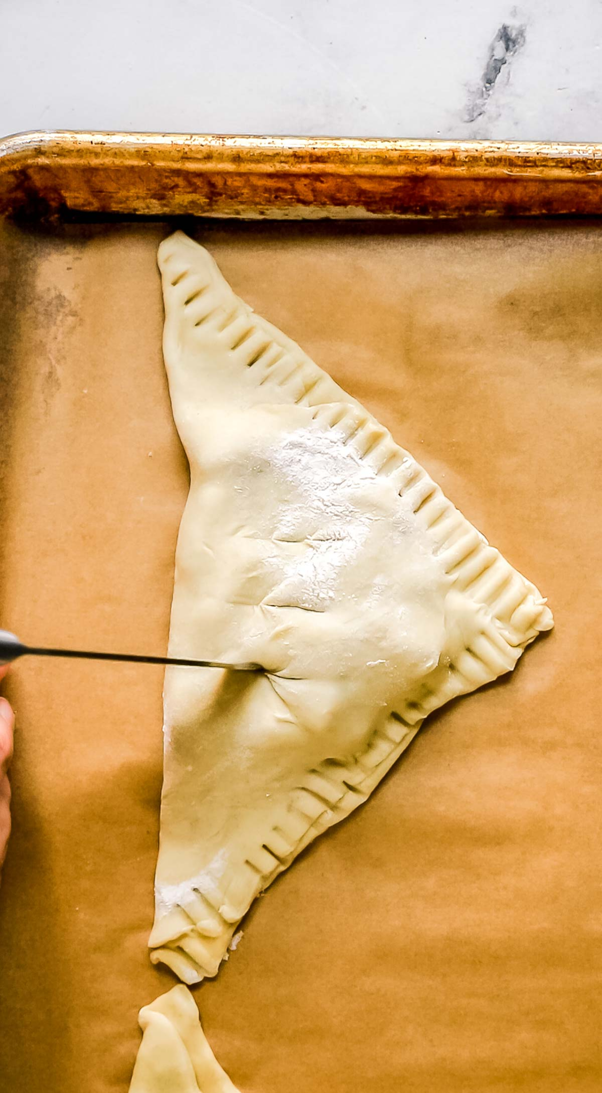 knife cutting slits into top of puff pastry apple turnover on parchment paper