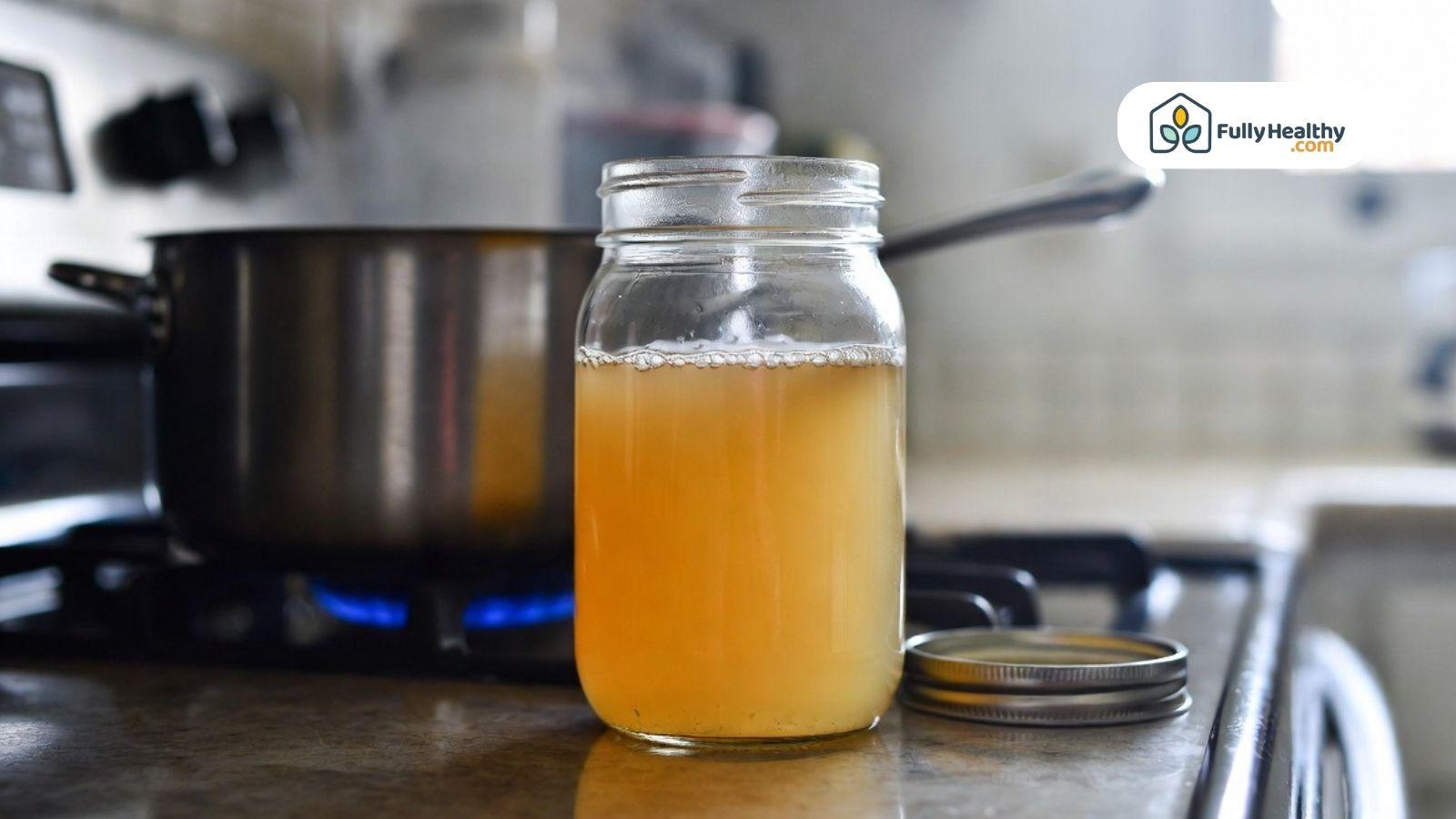 Homemade broth in a mason jar on a kitchen counter near a stove.