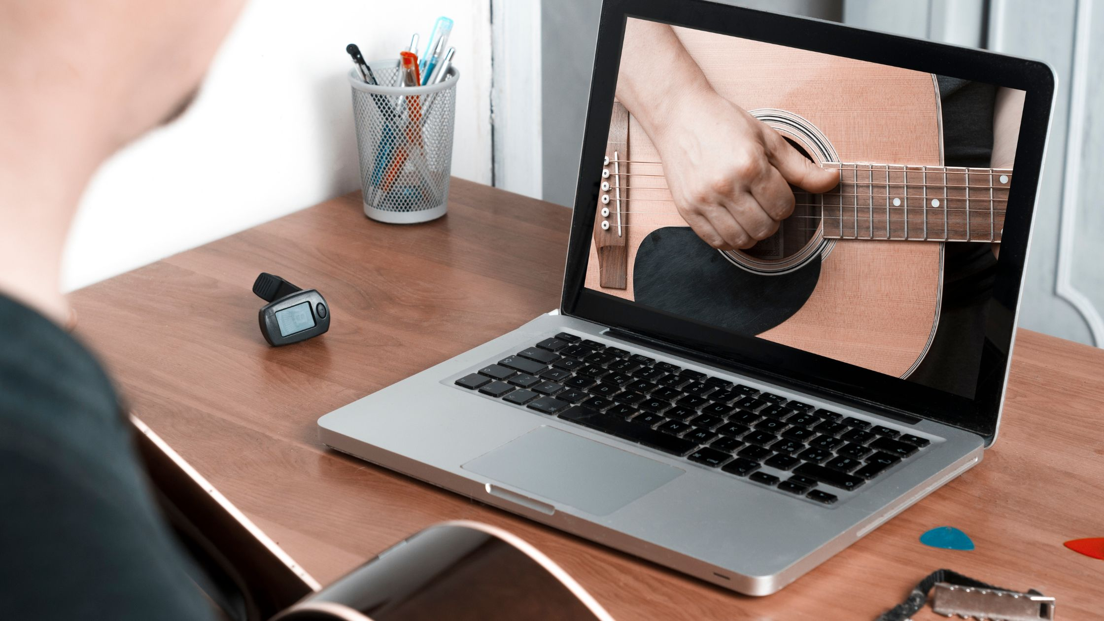teach yourself guitar is a best way to learn guitar - guitar player sitting in front of a laptop looking at an acoustic guitar