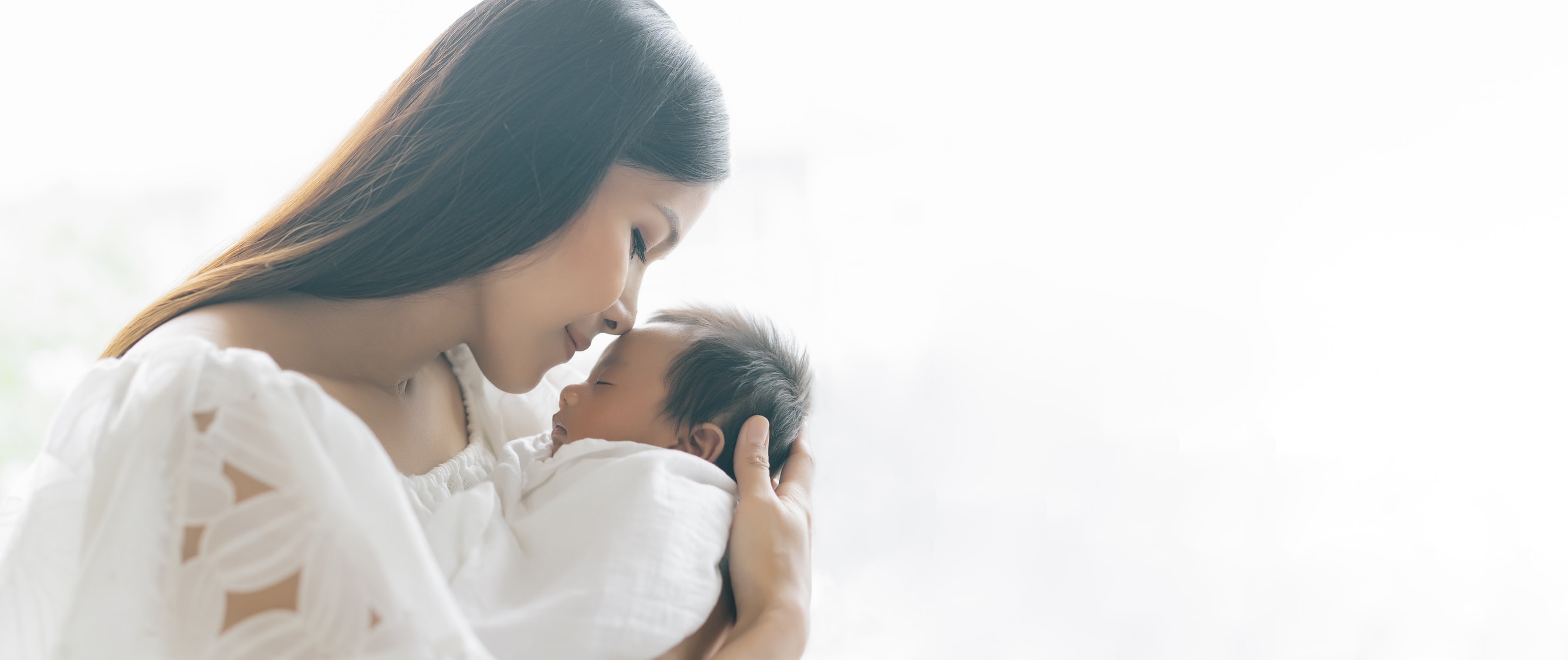 A new mother sitting on a couch in natural light, gently holding her infant and looking thoughtful, representing postpartum hormonal changes and healing