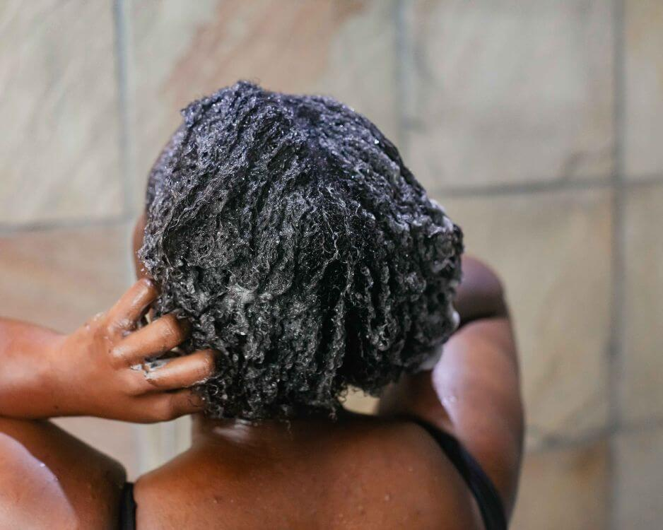 A woman with curly hair washing and conditioning her Cuban Twist Hair