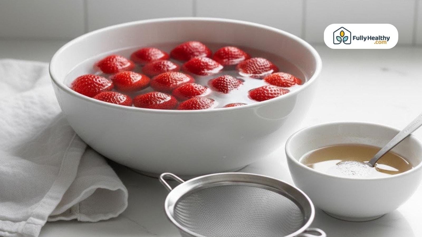 Fresh strawberries soaking in water bowl with strainer and vinegar solution nearby