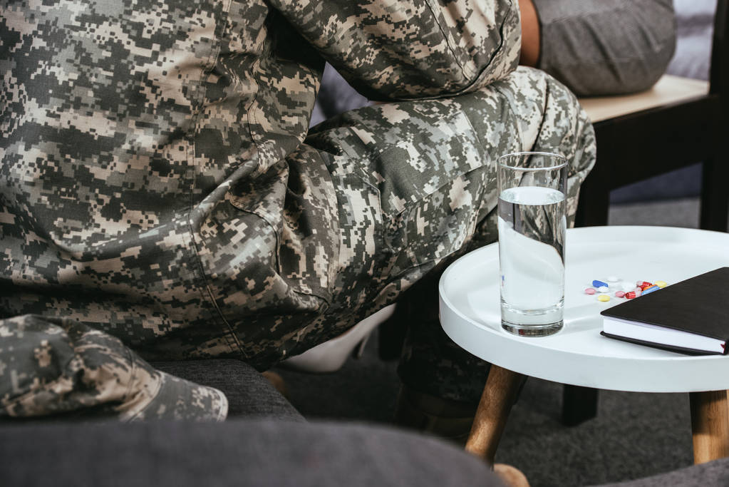 soldier sitting on couch with glass of water and pills on table