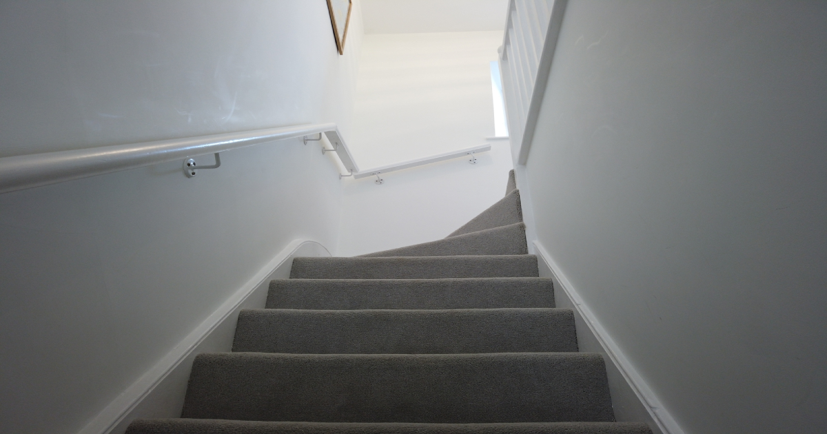 Het resultaat van een trap renovatie met grijs tapijt en witte muren.