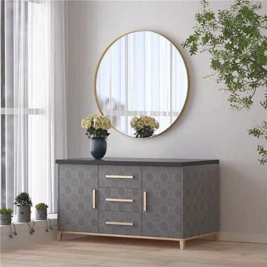Round wall mirror with thin brass frame above a modern gray sideboard in a bright, minimalist room.