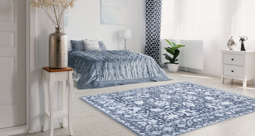 An Artiss Fafi rug is place at the foot of a pale blue bed in a mostly white bedroom. Using the rug here breaks up the monotony of the white carpet while also adding warmth and texture. 