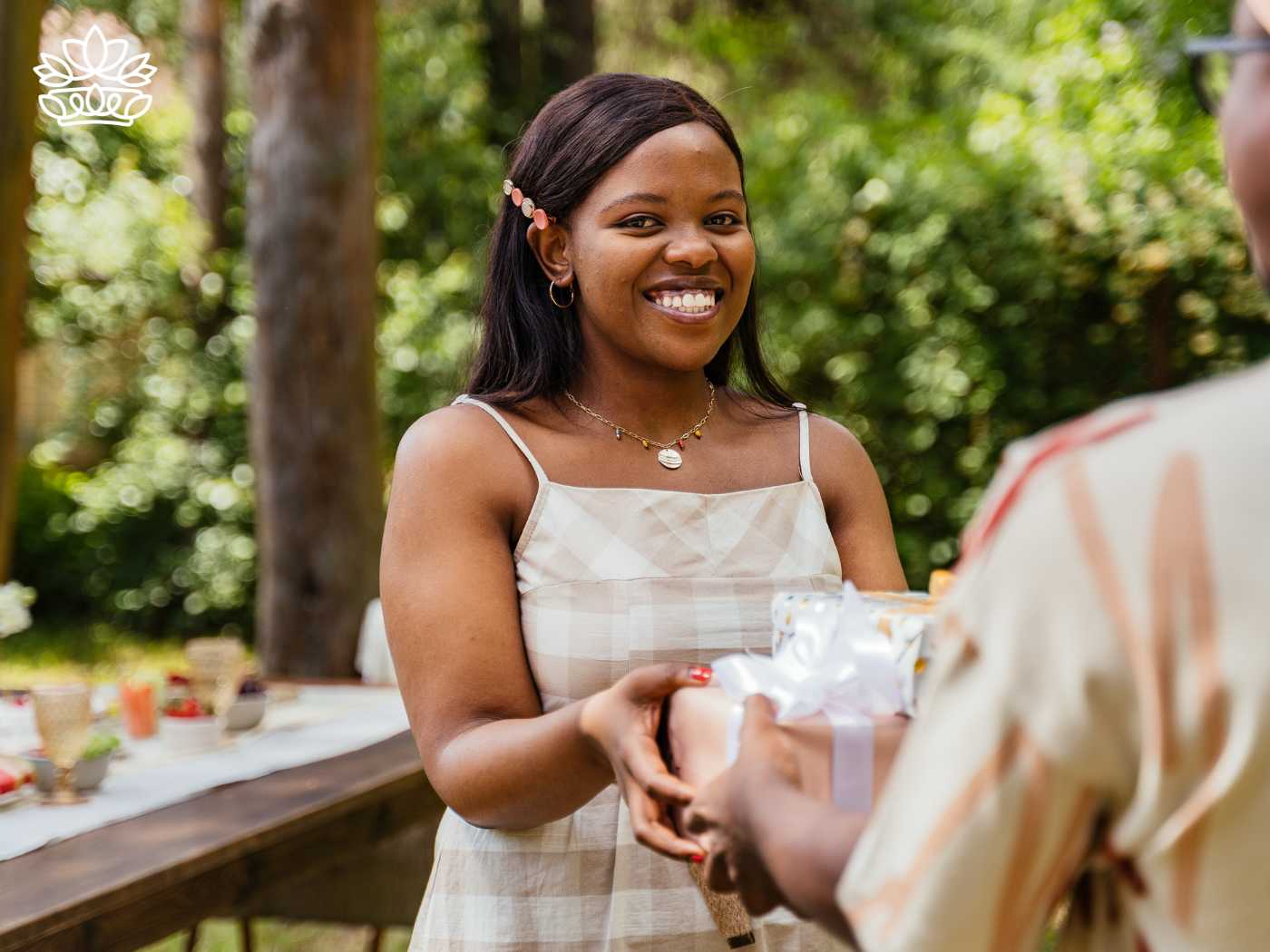 A smiling woman receiving a wrapped gift outdoors, from the Gifts Under R500 Collection at Fabulous Flowers and Gifts, including keywords such as order, colours, favourite, delivery, and birthday
