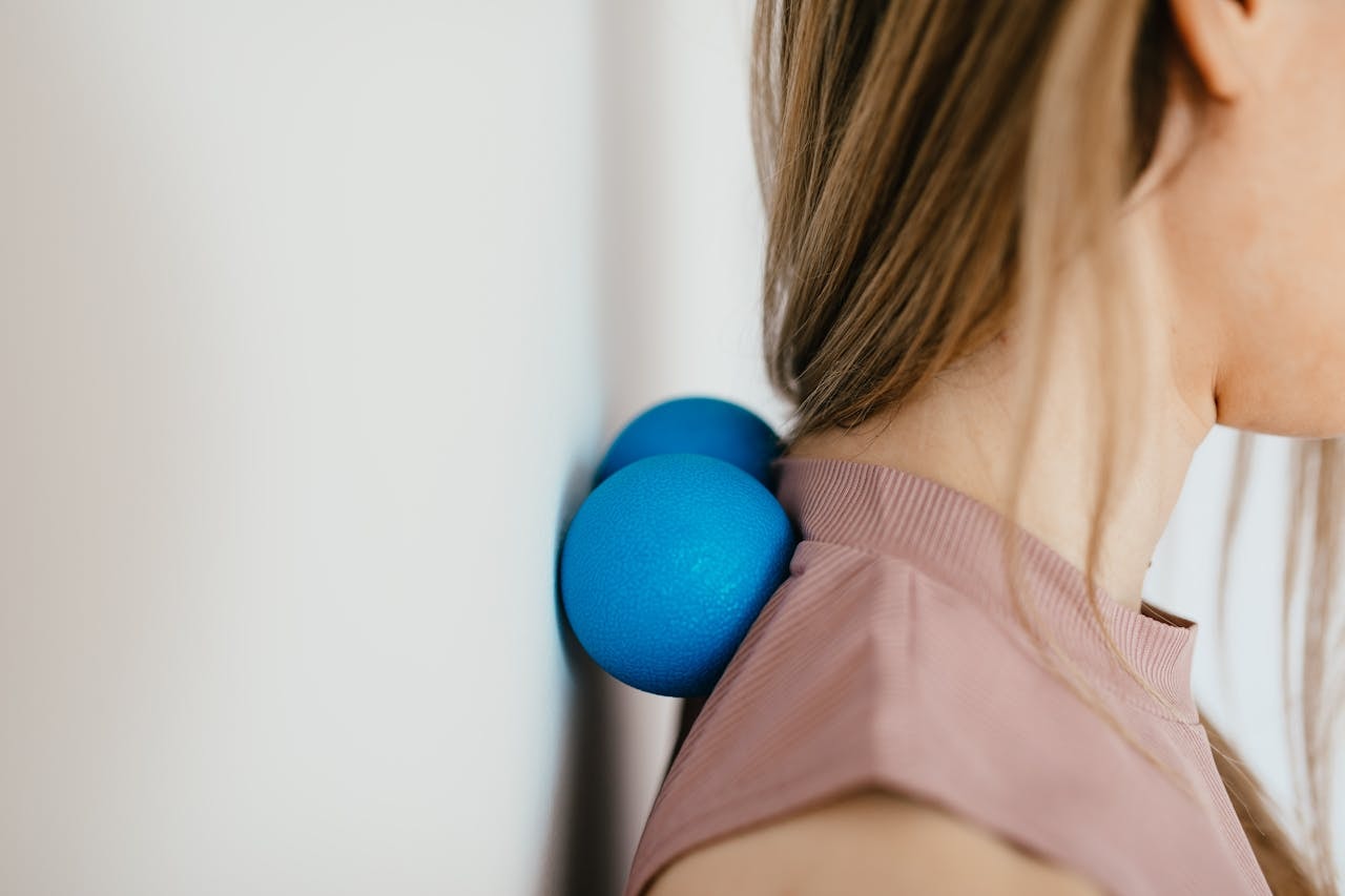 Self-massage with a double massage ball against the upper back near the neck to ease tight muscles and improve posture