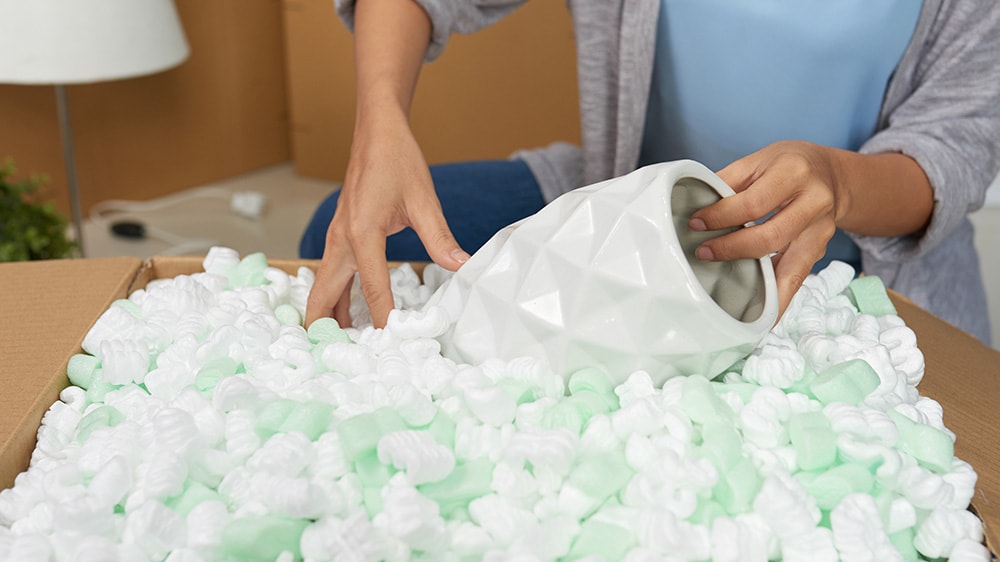 Women packaging a fragile vase with foam packing peanuts
