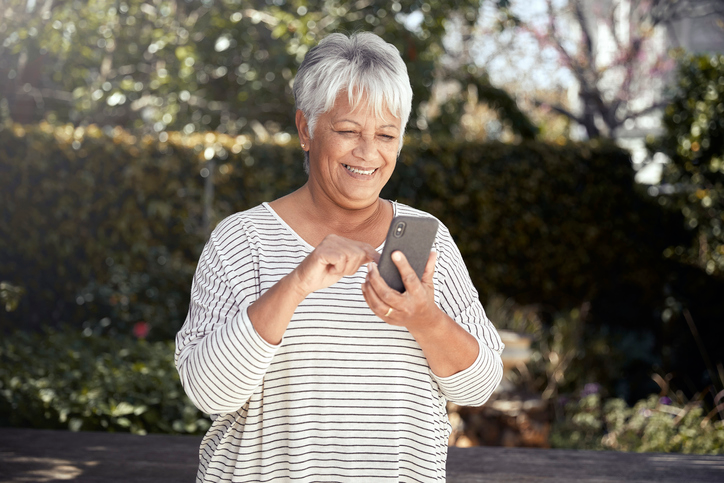 Happy older woman in a striped shirt sending a text. 