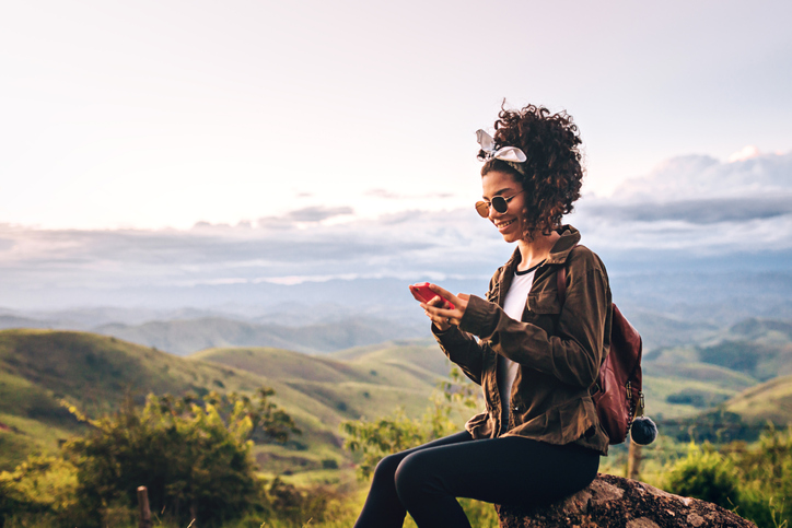 Happy young woman taking a break from hiking to check her cell. 