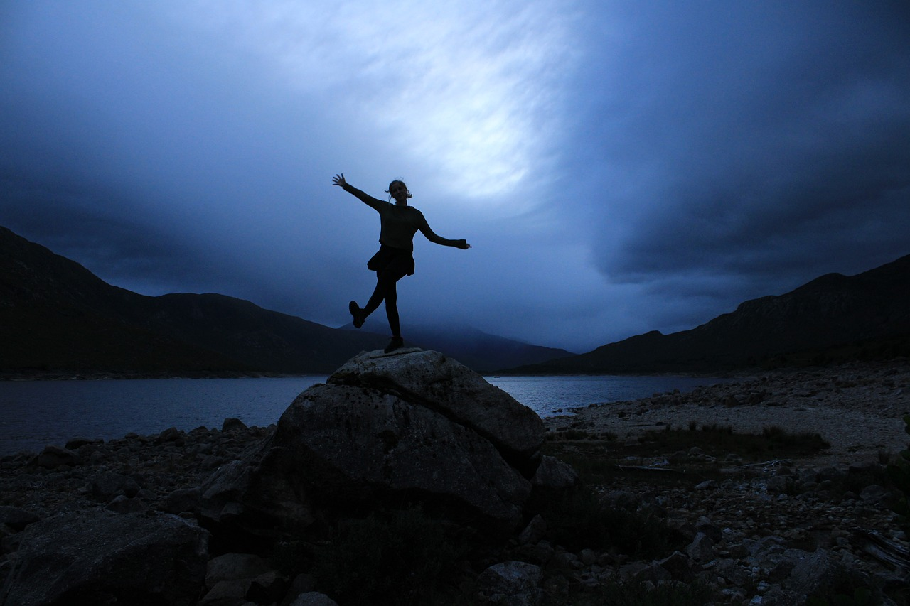 Woman dancing on boulder in the moonlight next to a river. 