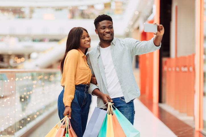 Happy young couple holding brightly colored shopping bags. 