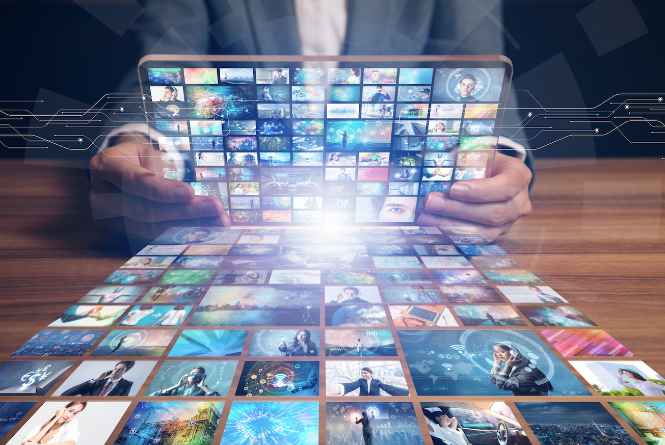 a person holding a tablet with online video screens across it as it reflects agains the wooden table below