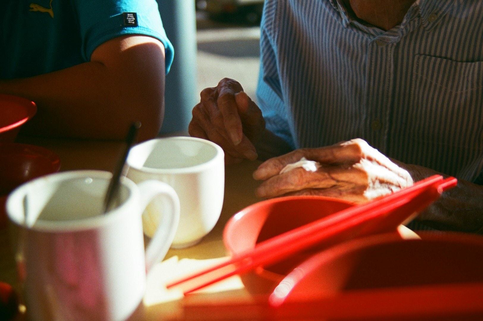 A man sitting at a table in a Singapore hawker center, enjoying a cup of coffee.