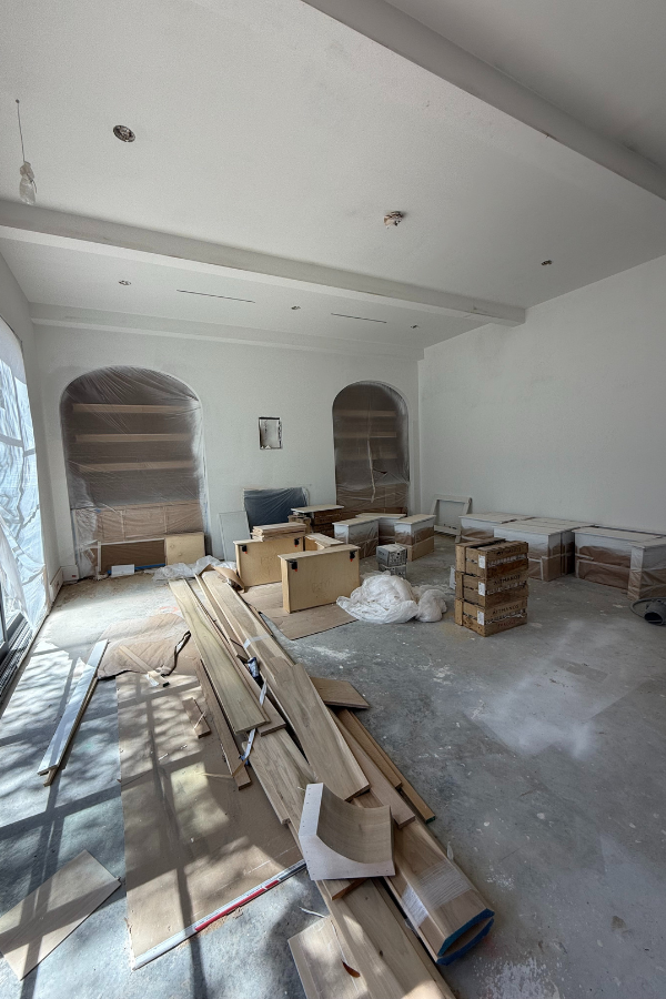 A construction site in progress with unfinished floors, wooden boards, and cabinetry materials spread out in a partially built interior room.