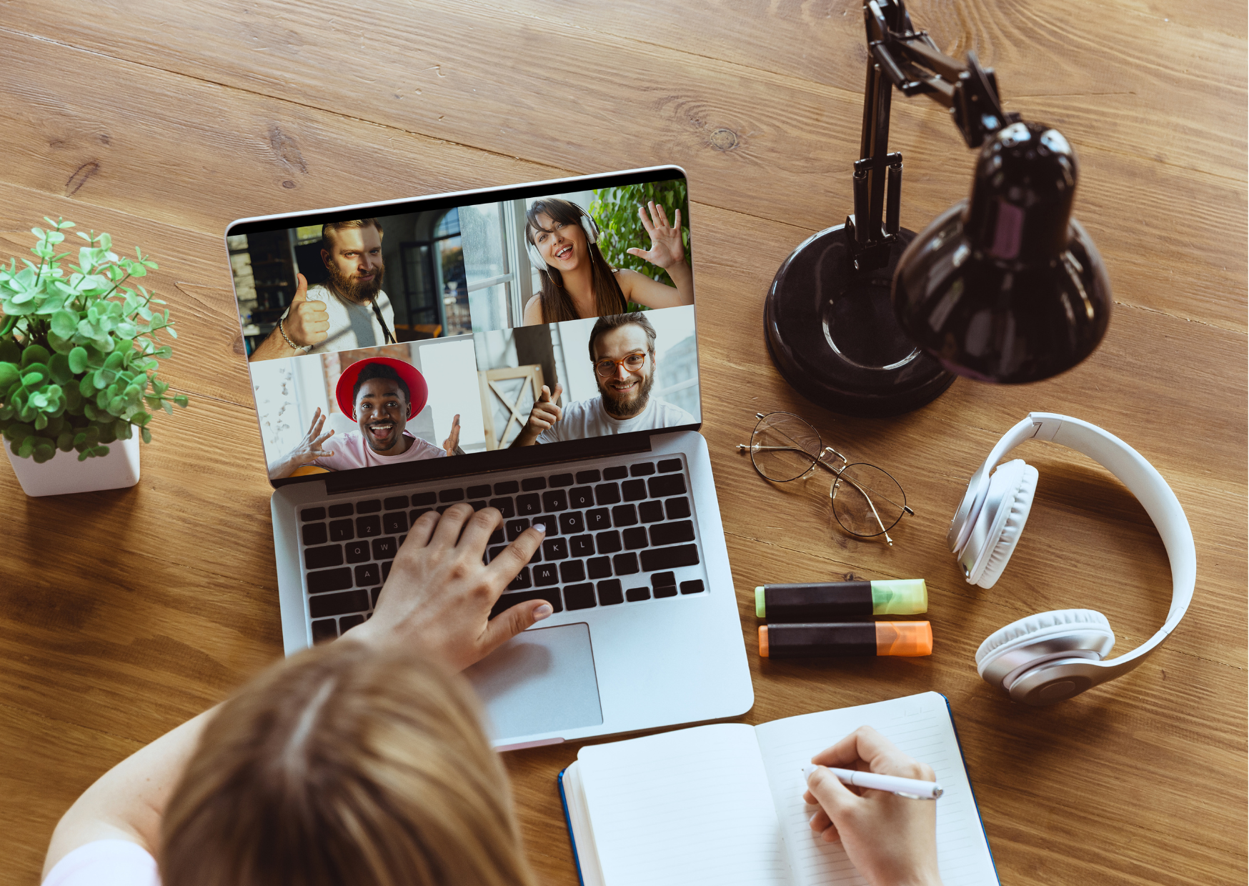 Overhead view of a person taking notes while on a video call with four participants displayed on a laptop screen.