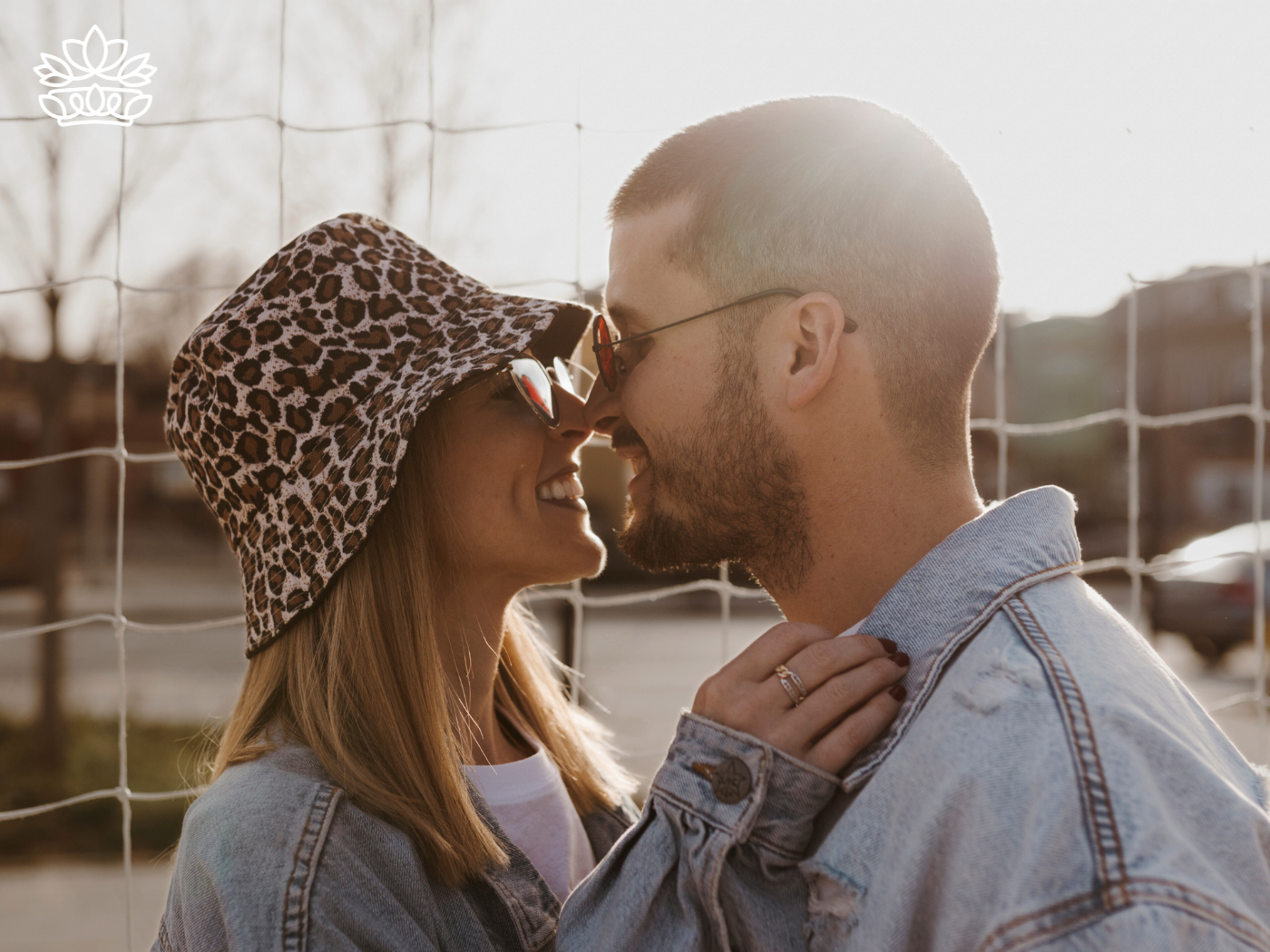 A couple smiling at each other in an intimate moment, wearing sunglasses and denim jackets, as the sun shines brightly behind them. Fabulous Flowers and Gifts. Gift Boxes for Boyfriend. Delivered with Heart.