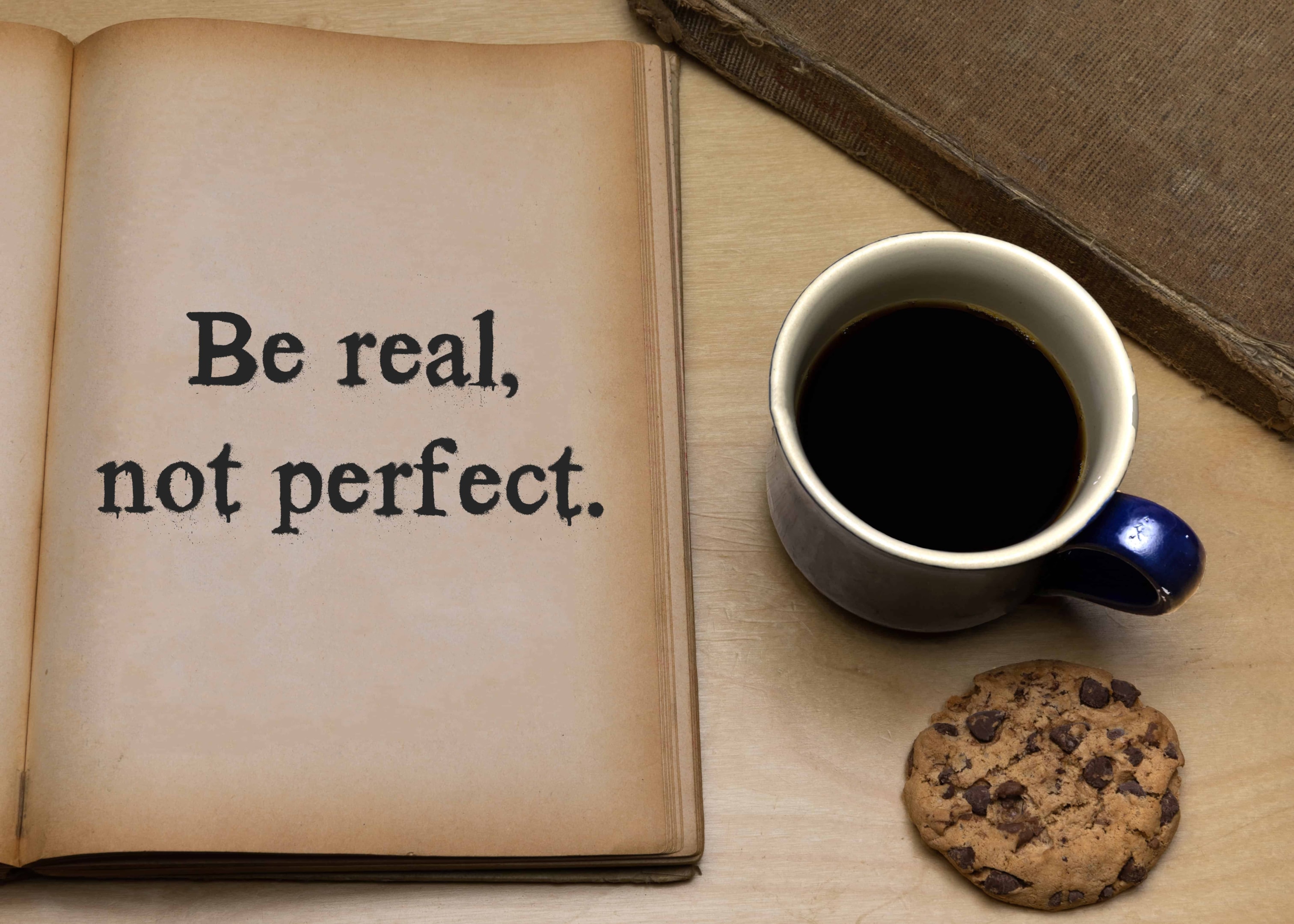 A book with a page open that says be real not perfect emphasizing the importance of authenticity for a happy life.