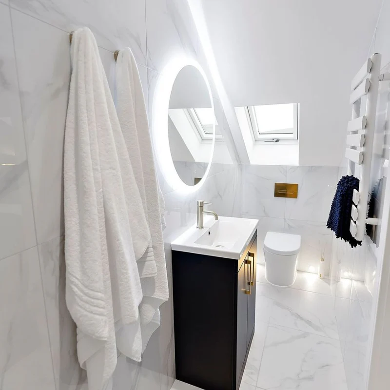 Attic bathroom with marble-effect tiles, a backlit oval mirror, skylight windows, and a sleek vanity unit.