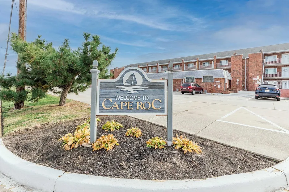 Welcome sign for Cape Roc Rentals in Cape May, New Jersey, with the brick condo complex visible in the background.