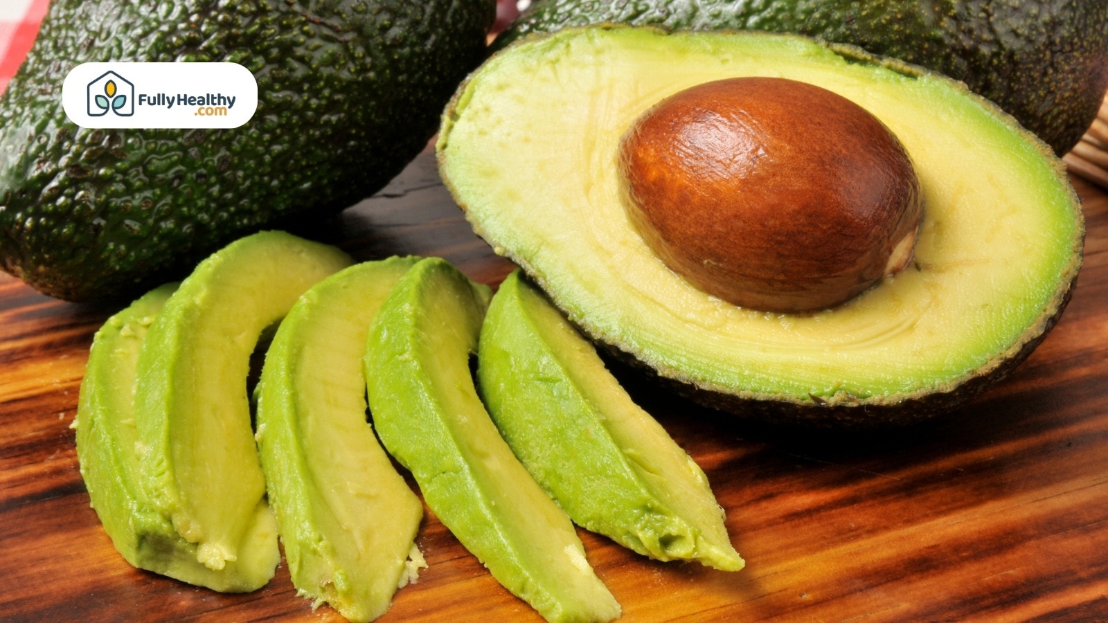 Fresh avocado slices and halved avocado with seed on wooden board