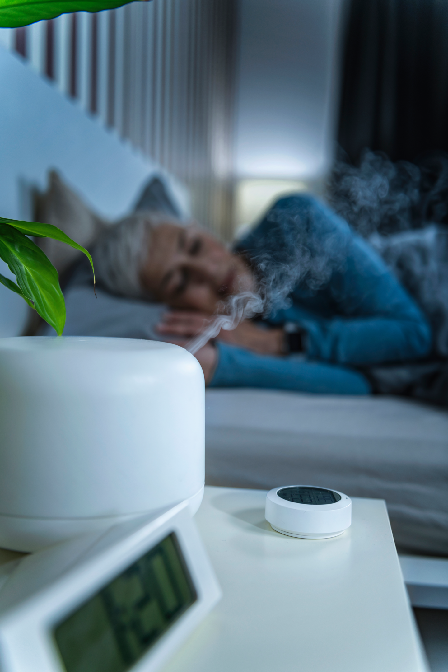 An image of a woman sleeping in bed with a humidifier on her nightstand to ease menopause throat and mouth symptoms. 