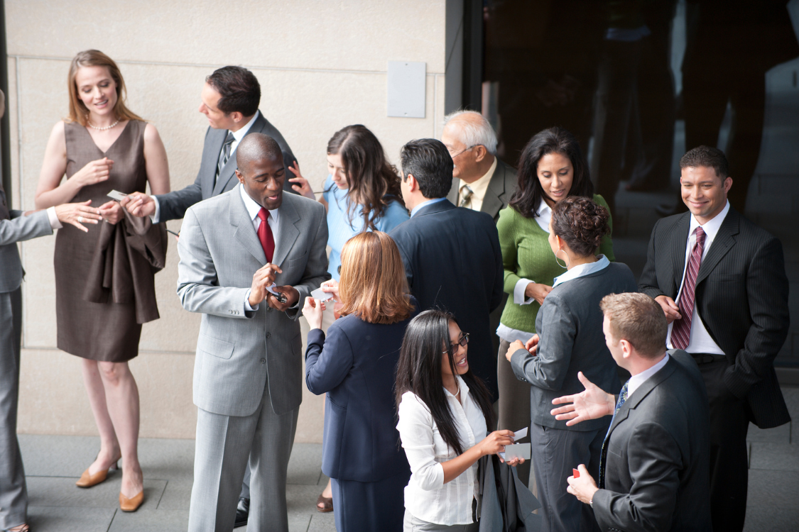 Professionals exchanging business cards and networking at a business event, building connections to find trusted brokers through referrals.