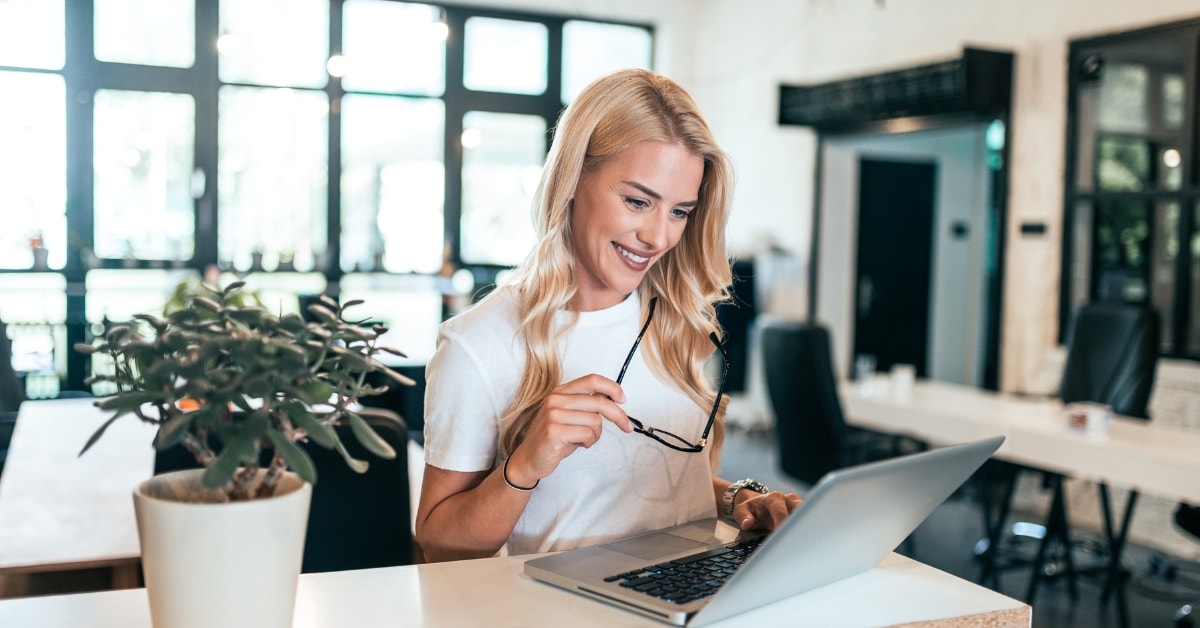 A smiling woman working on her laptop in a modern office, seeking information about the OnlyFans SETC tax credit.