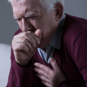 An image of a senior man with his fist over his mouth clearing his throat. 