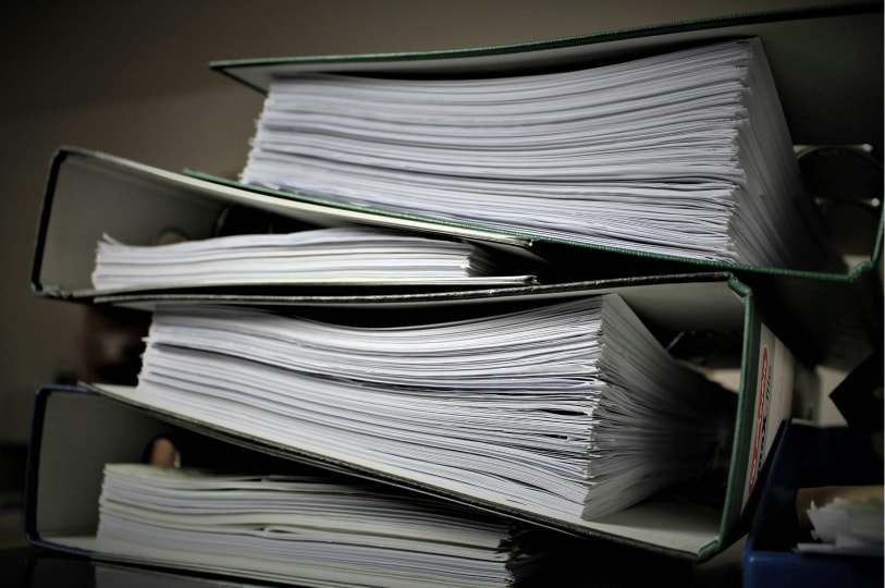 A stack of three green ring binders overstuffed with white documents.