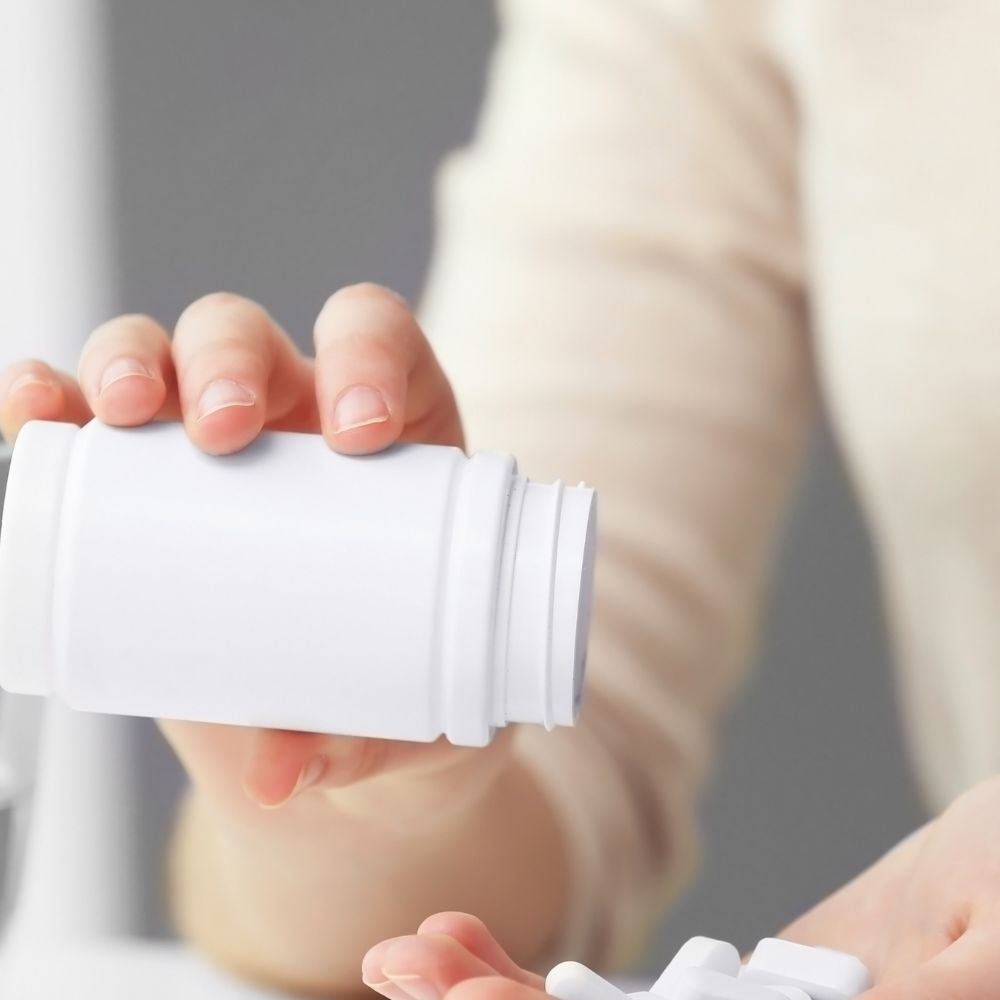 A person holding a bottle of vitamin E supplements, highlighting the importance of vitamins for preventing liver disease.