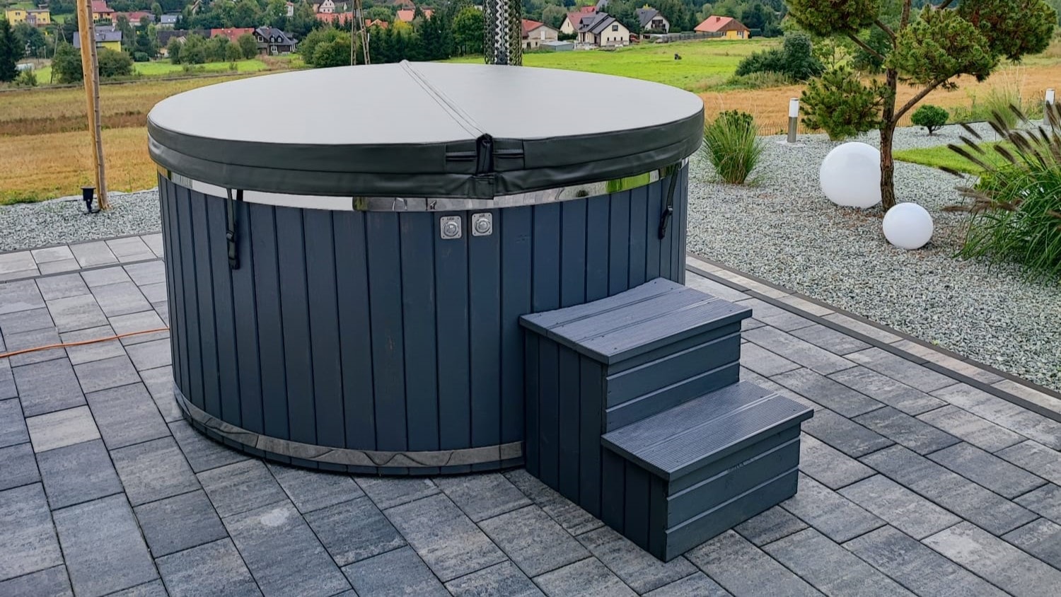 Zdjęcie poglądowe przykładowej balii ogrodowej. Konstrukcja wykonana z drewna świerkowego lub modrzewia chroni przed wilgocią i zapewnia długotrwałe użytkowanie. Elementy ze stali nierdzewnej, jak komin czy osłona komina, gwarantują bezpieczeństwo i trwałość.