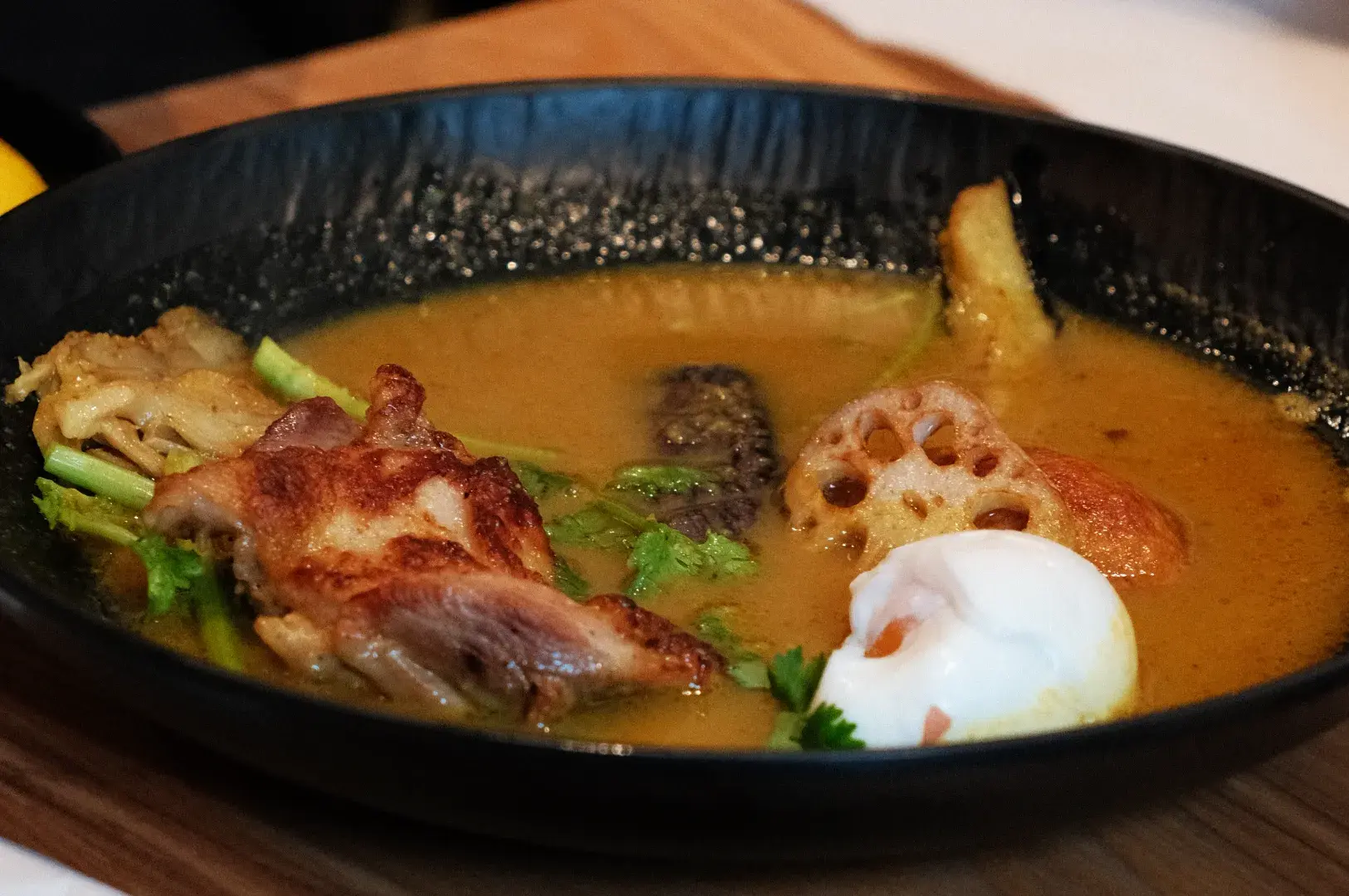 A bowl of soup with chunks of meat, vegetables, and a poached egg.